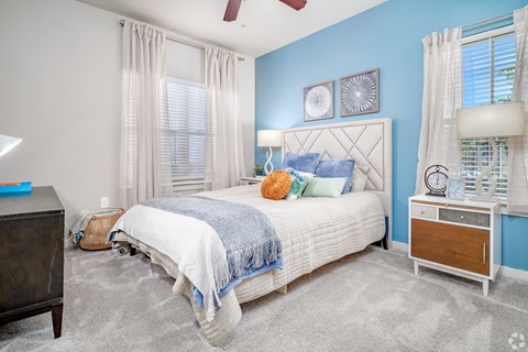 A bedroom with a white bed, blue walls, and a ceiling fan.