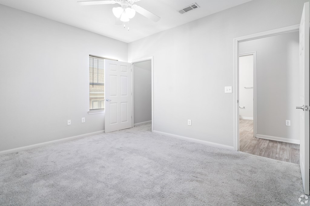 A spacious room with a carpeted floor and a ceiling fan.