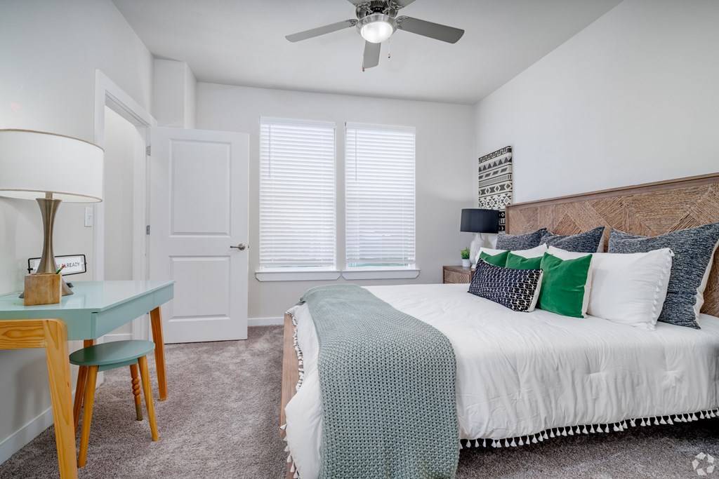 A bedroom with a bed, a table with a lamp, and a ceiling fan.