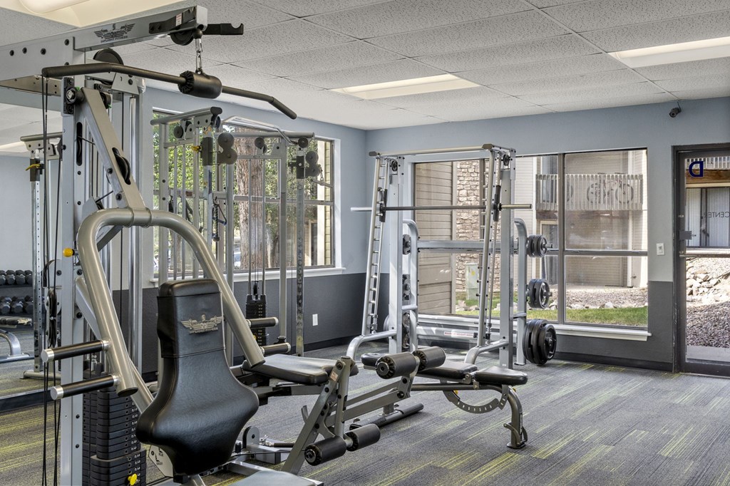 A gym with a variety of equipment including a weight bench, a cable machine, and a squat rack.