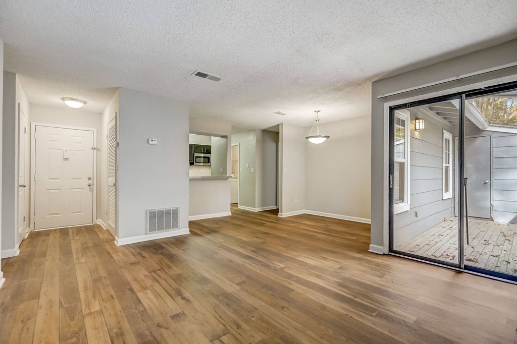 a view of the living room and kitchen with white walls and hardwood floor with a door to a private outdoor balcony at Veridian at Sandy Springs