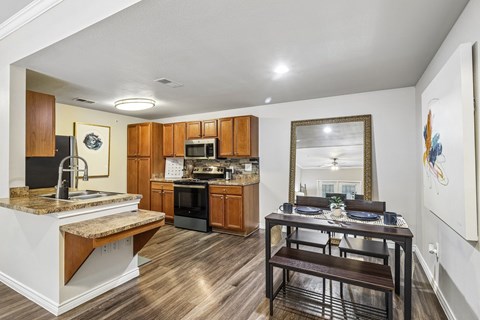 A kitchen with a table and chairs in the foreground and a counter with a sink in the background.