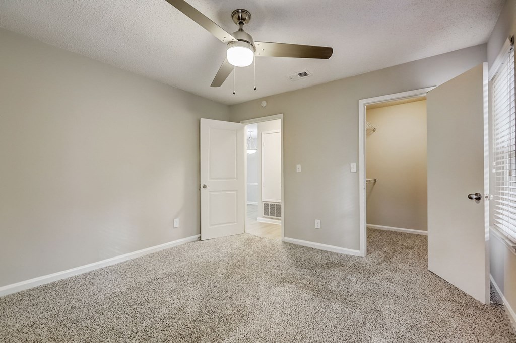 an empty living room with a ceiling fan and a door to a bathroom