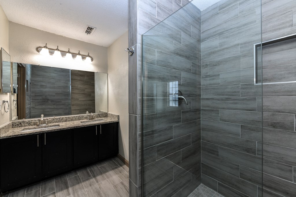 Modern Bathroom with a Grey-Tile Shower, Granite Double-Sink Vanity, a Large Mirror, and Black Cabinets