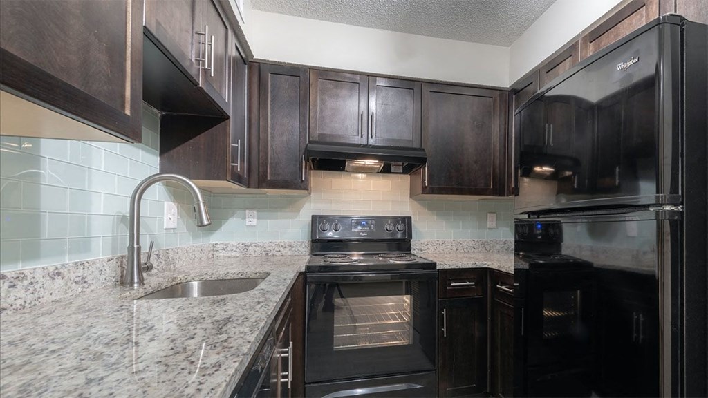 Amberlake Village's kitchens are designed with Granite Countertops, Tile Backsplash, Dark Wood-Style Cabinetry, and Black Appliances