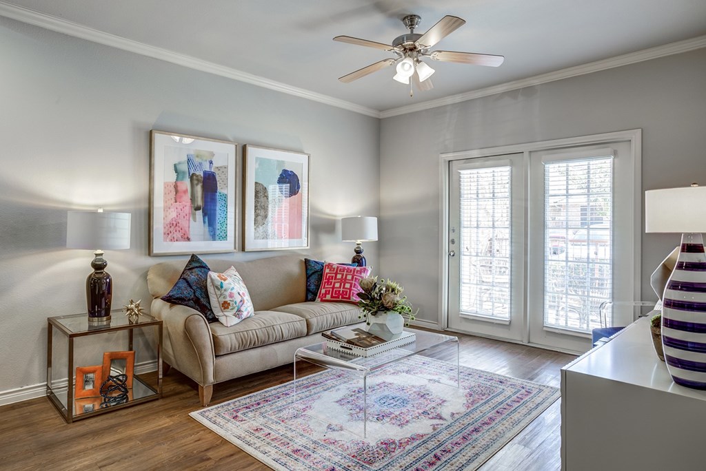 A living room with a beige couch, a glass table, and a ceiling fan.