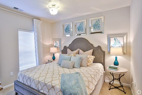 A bedroom with a large bed and a small table with a lamp on it.