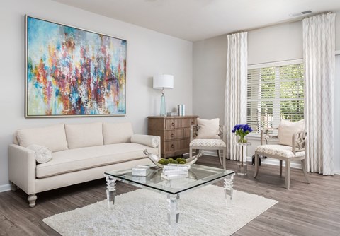 A living room with a white couch, a glass coffee table, and a colorful painting on the wall.