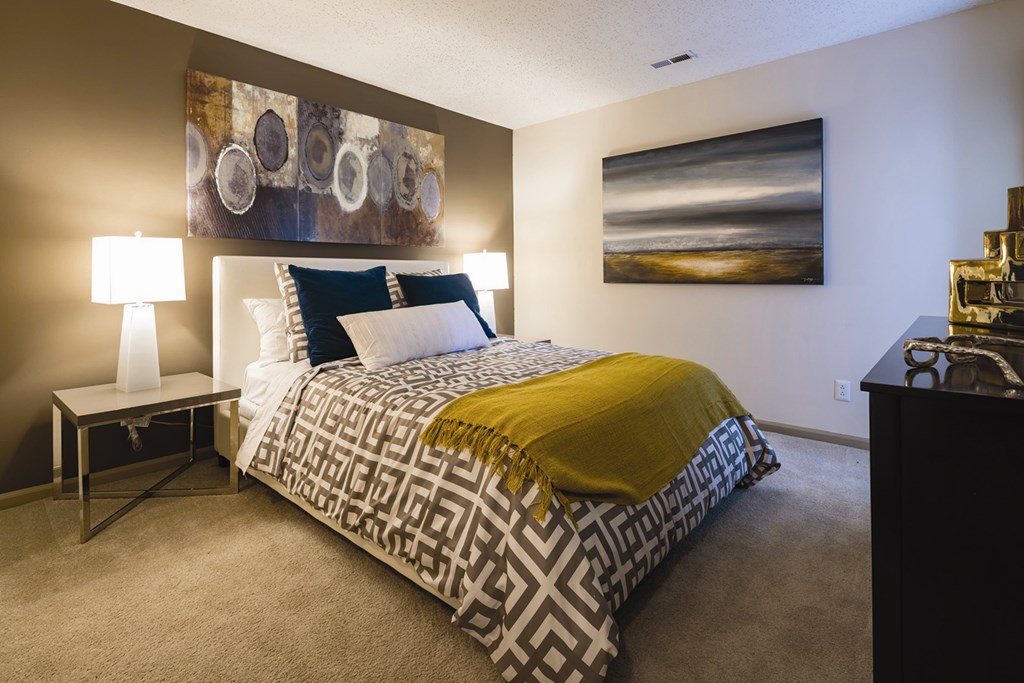 A bedroom with a bed, nightstand, and a painting on the wall.