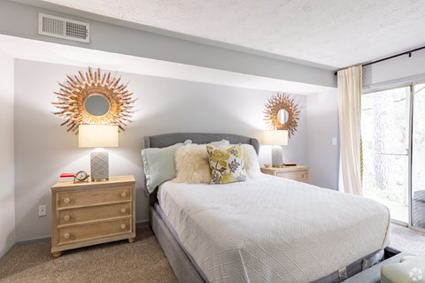 A bedroom with a large bed, a nightstand with a lamp, and two sunburst mirrors on the wall.