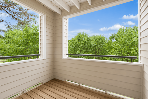 A sunny day with a view of green trees from a wooden balcony.