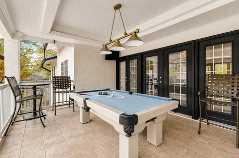 A pool table is in the middle of a room with a bar and chairs.