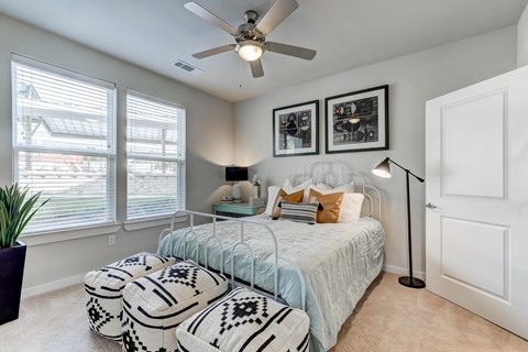 Dog-Friendly Luxury Apartments in North San Antonio, TX - Hardy Oak - Bedroom With Large Windows, Ceiling Fan, Ottomans, Lamps, Wall Art, and Modern Decor.