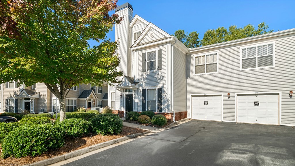 a white house with a driveway and a tree in front of it