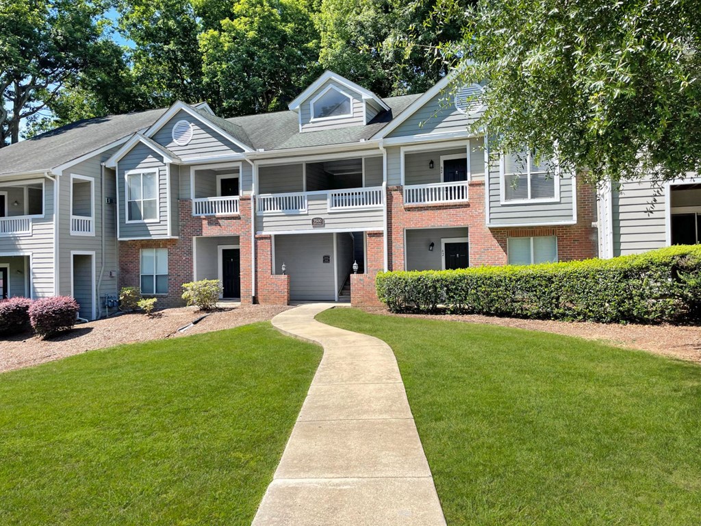 a walkway leading to an apartment building with a lawn