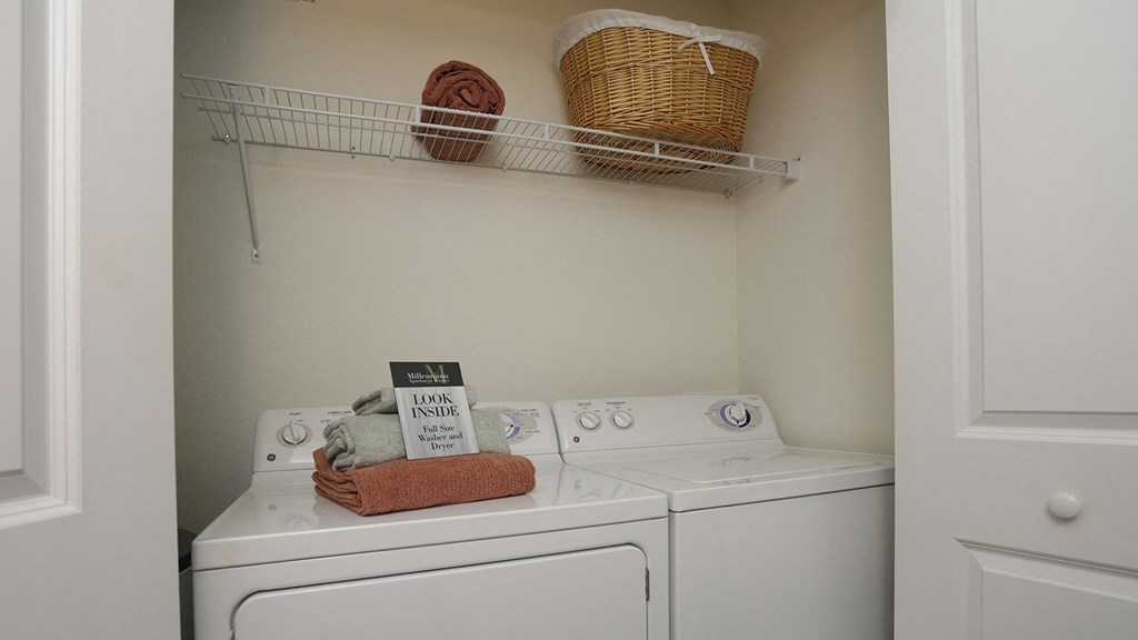 A small laundry room with a washer and dryer and a basket on the shelf.