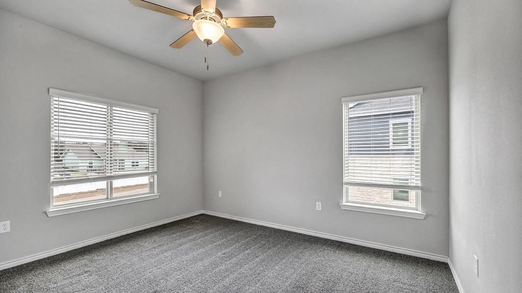an empty bedroom with a ceiling fan and two windows