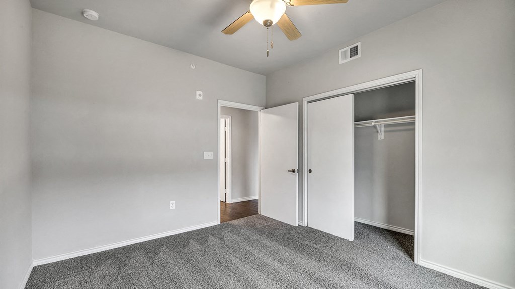 an empty bedroom with a ceiling fan and closet
