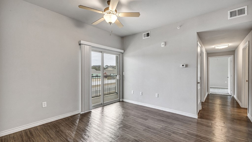 an empty living room with a ceiling fan and a balcony