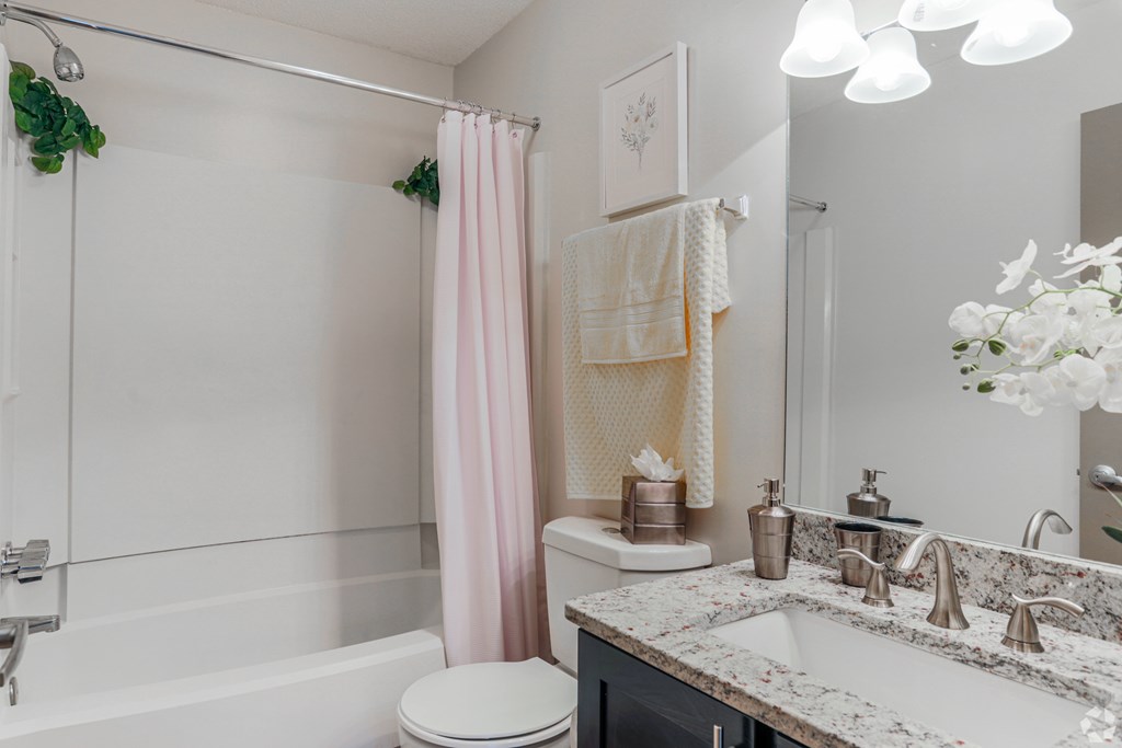 A white walled bathroom with granite countertops, a tub shower, and a pink shower curtain.