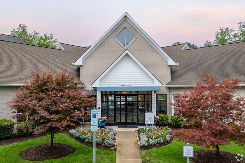 The leasing office with a white roof and a glass door is surrounded by trees and bushes.