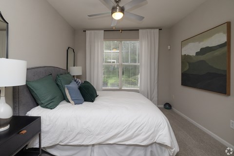 A bedroom with a bed, a ceiling fan, and a painting on the wall.