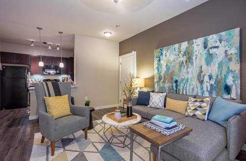 A living room with a grey couch, a yellow pillow, a grey armchair, a coffee table, and a painting on the wall.
