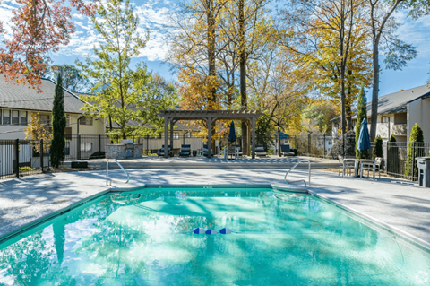 Buckhead, GA, Garden-Style Apartments Near Midtown Atlanta - 55 Pharr - Swimming Pool With Clear Water, Lounge Seating, Pergola, Outdoor Grill, Apartment Buildings, and Tall Trees.