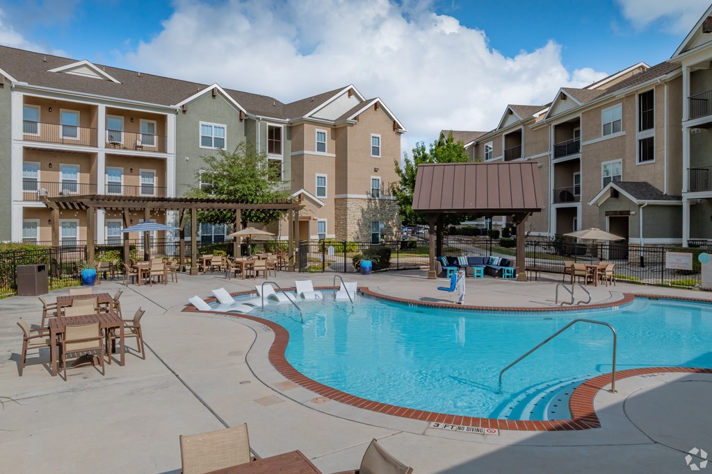 A large swimming pool surrounded by a patio with chairs and umbrellas.