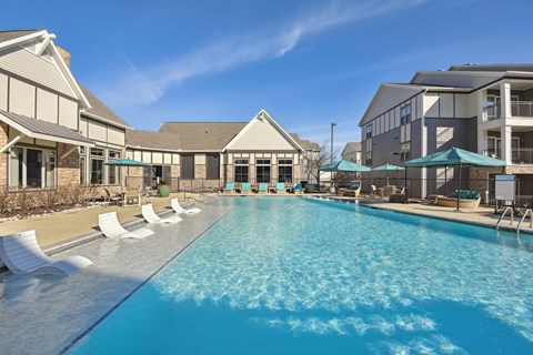 a swimming pool with chairs and umbrellas in front of a building with apartments