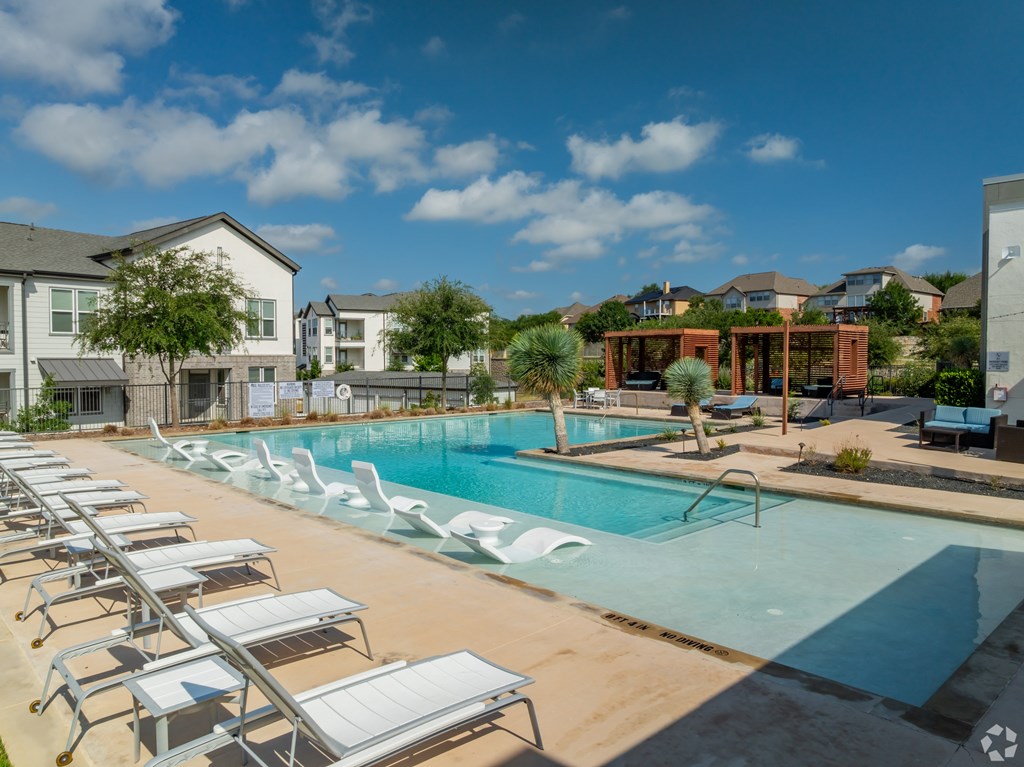 A pool with sun loungers and a building in the background.