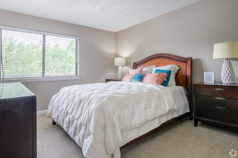 A bedroom with a large bed and a window with blinds.