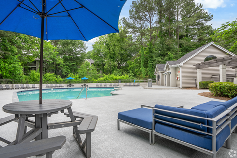 Two-Bedroom Garden-Style Apartments in Smyrna, GA - The Emerson 1600 - Resort-Style Swimming Pool With Blue Umbrellas, Picnic Tables, Lounge Seating, Spacious Sundeck, and Surrounding Trees.
