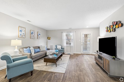 A living room with a blue chair, a grey couch, a coffee table, a flat screen TV and a wall with pictures and a decoration.