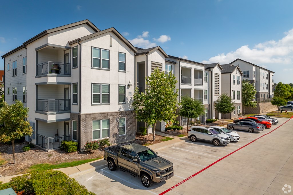 A row of apartment buildings with cars parked in front.
