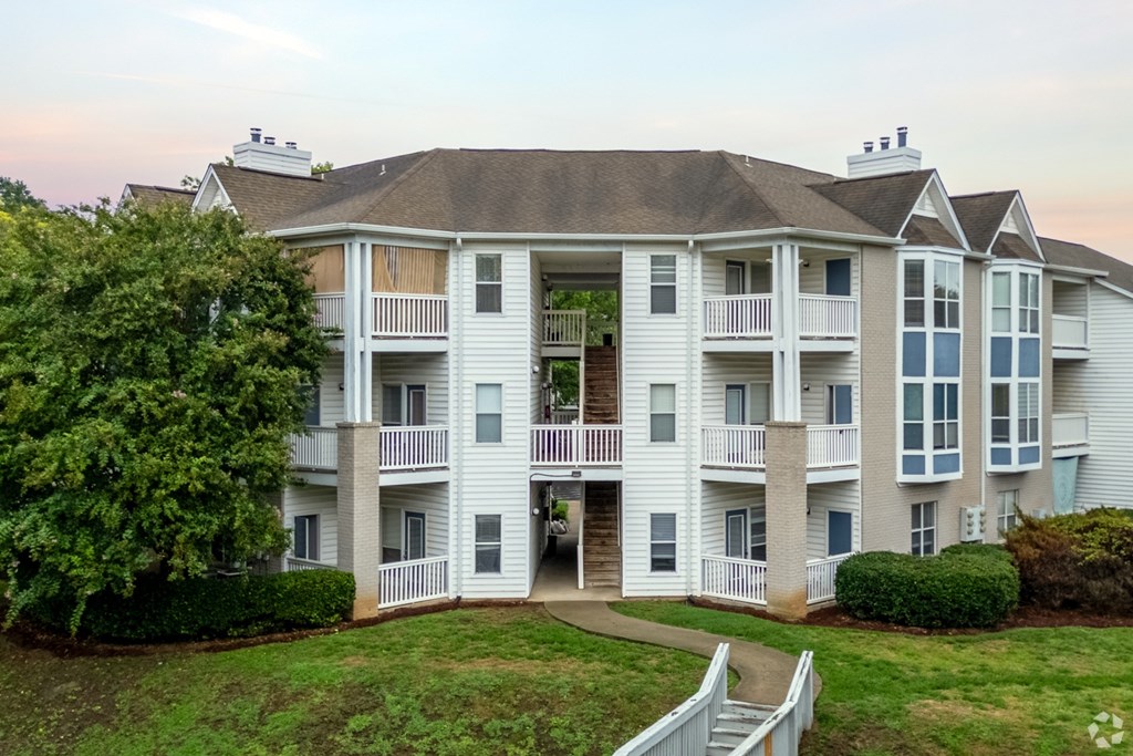 A large white apartment building with a balcony and a staircase leading to the entrance.