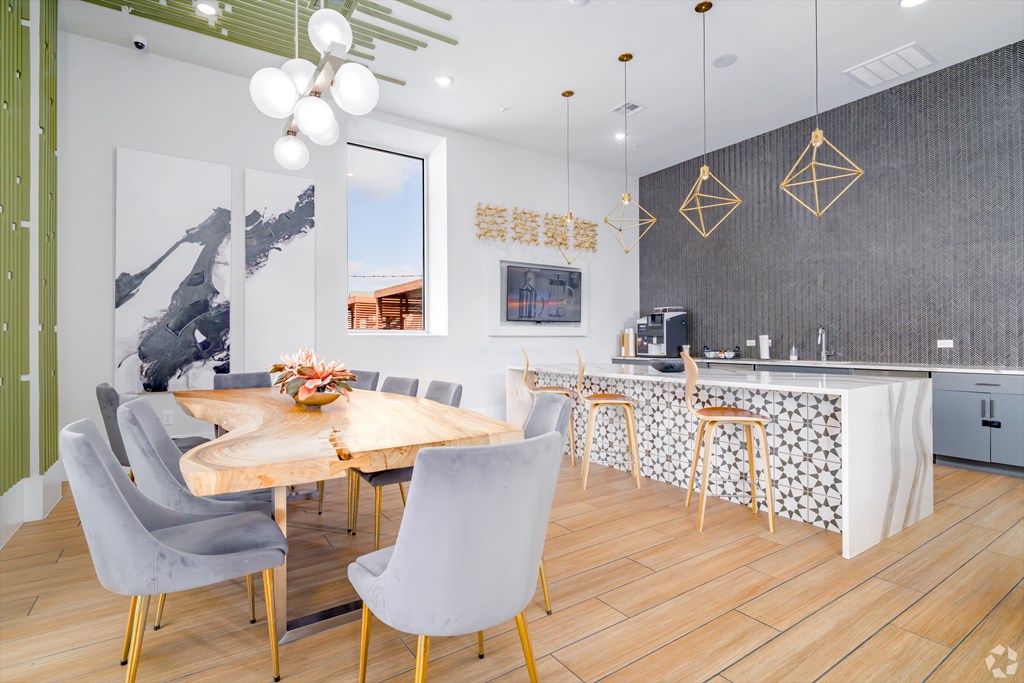 A modern community kitchen and dining room with a wooden table and grey chairs.