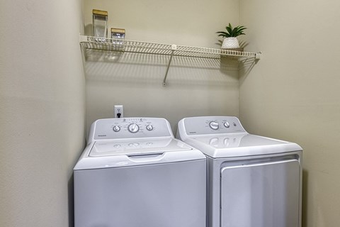 a washer and dryer in a laundry closer with a shelf above them at Wynnwood Vinings apartments