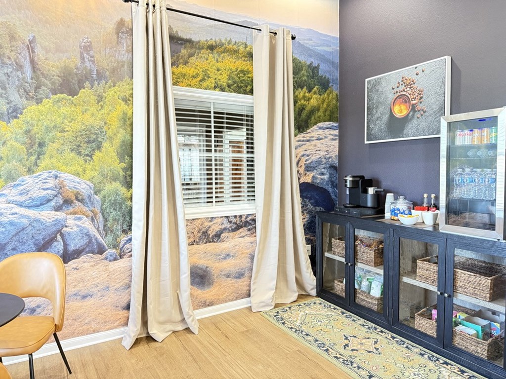 A room with a large mural of a landscape behind a window with beige curtains.