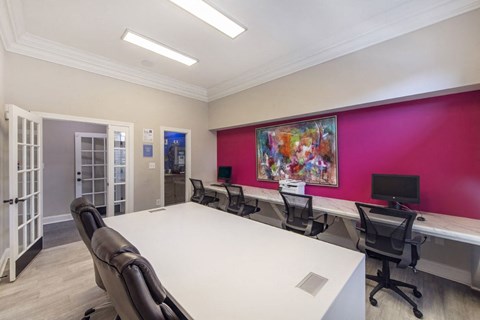 A conference room with a white table and chairs, a pink wall, and a painting on the wall.