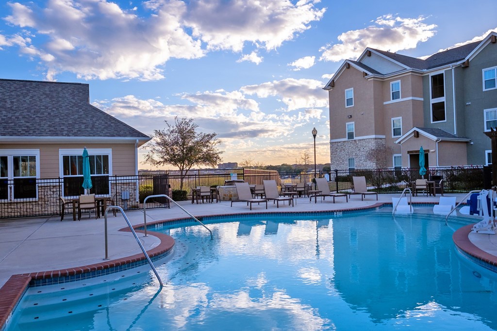 A swimming pool in front of a building with a sunset in the background.