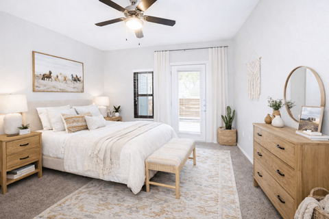 3-Bedroom Apartments in Churchill Estates, TX - Apex Apartments - Bedroom With White Bedding, Wood Furniture, A Ceiling Fan, Soft Area Rug, And Glass Door.