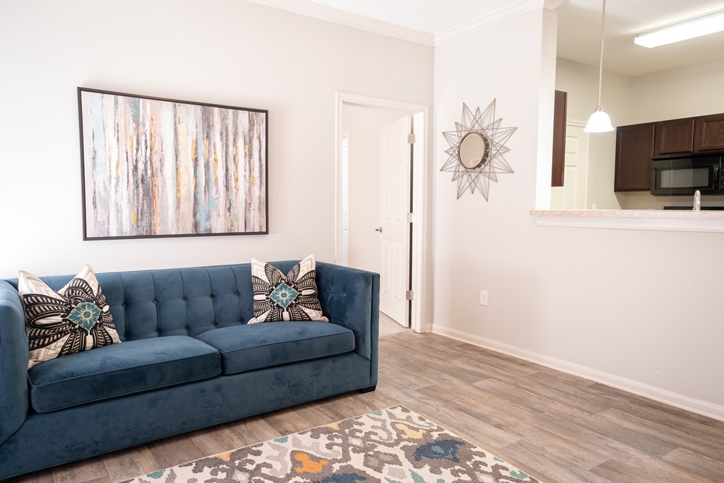 A blue couch with two pillows sits in a room with a white wall and a painting hanging above it.