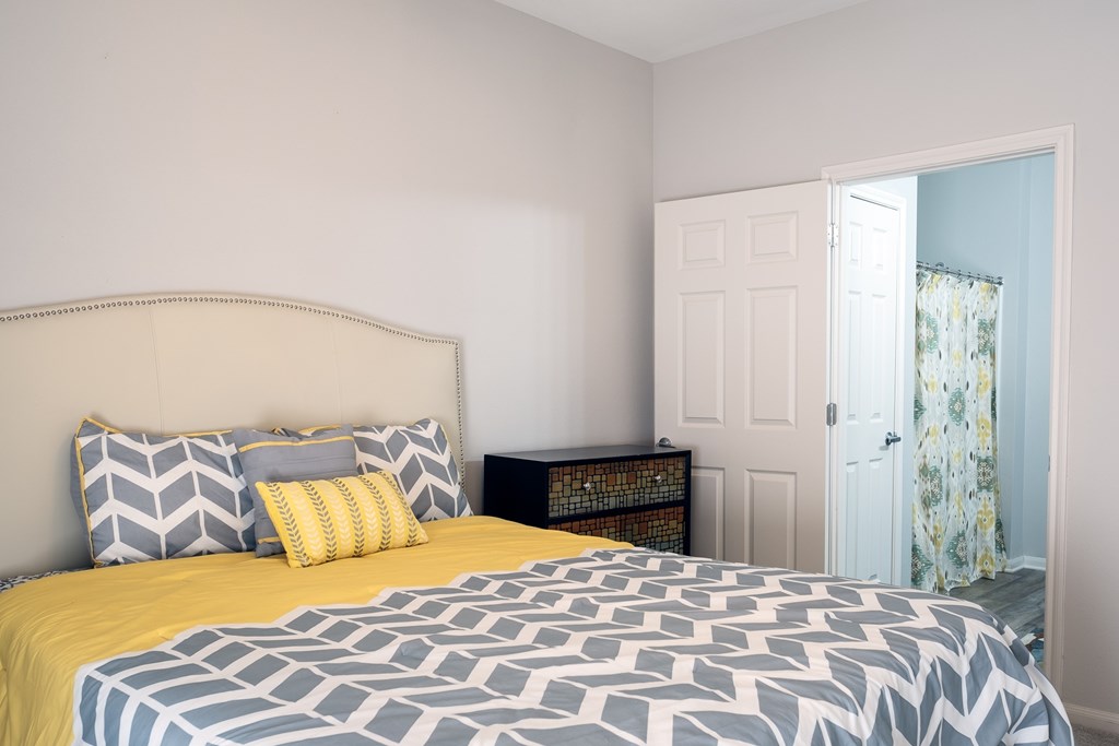 A bed with a yellow comforter and grey and white patterned duvet cover.
