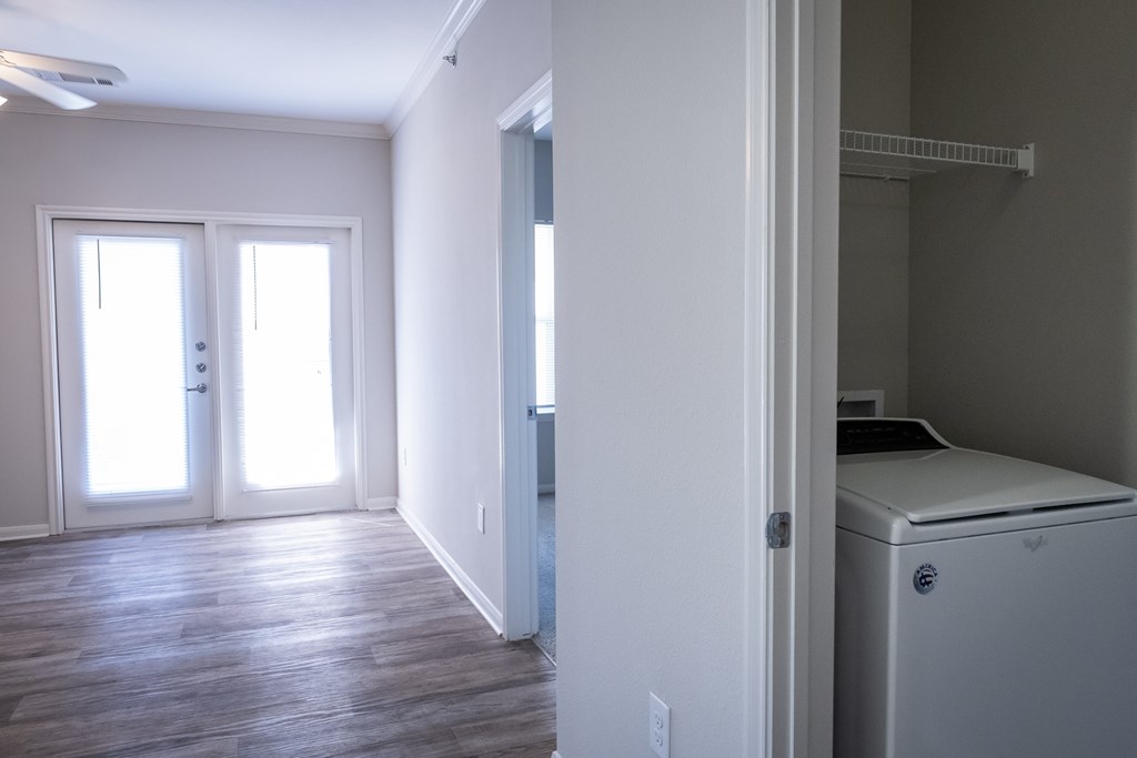 A white washing machine is in a small room with wood floors and white walls.