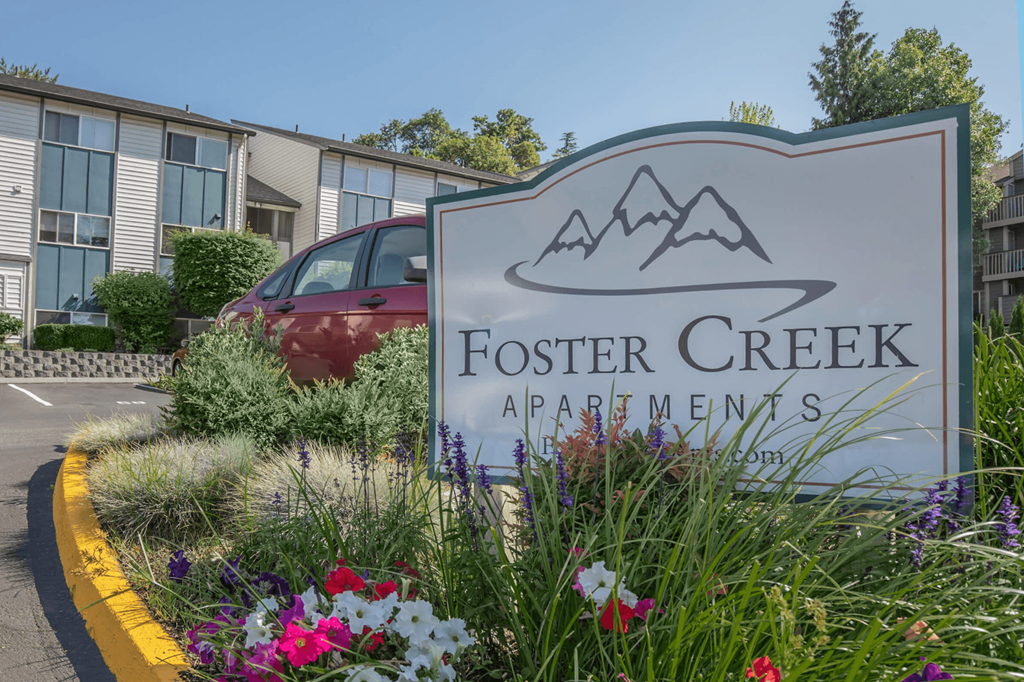 A sign for foster creek apartments with flowers in front of it