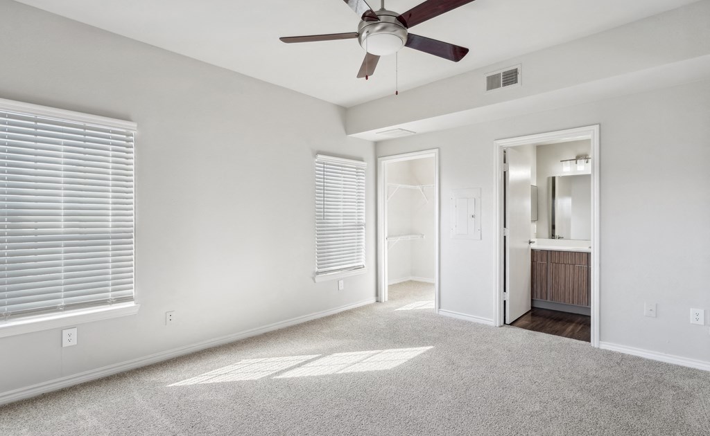 an empty living room with a ceiling fan and a door to a bathroom