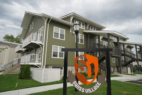 A sign for Swiss Village stands in front of apartment buildings.