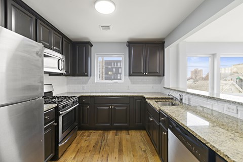 A kitchen with black cabinets and a stainless steel refrigerator.