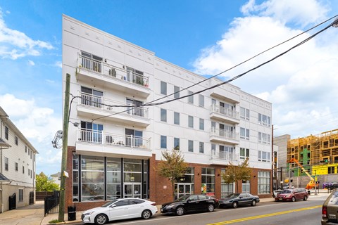 A white building with balconies is in the foreground with cars parked in front.